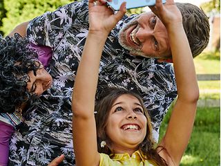 Eine Momentaufnahme einer lachenden Familie, die gerade mit dem Smartphone ein Selfie macht.