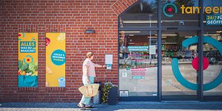 Frau mit Einkaufstasche öffnet Supermarkttür mit Zugangskarte.