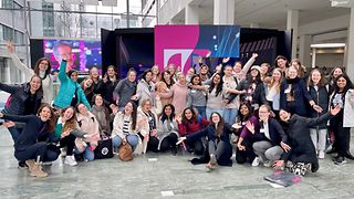 A large group of women looks into the camera, smiling and cheering.