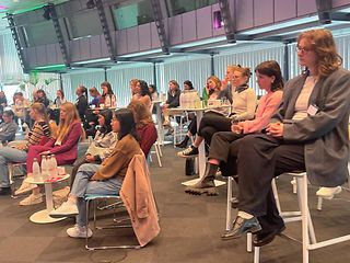 Young women sit in rows in a large Telekom room and follow the presentations